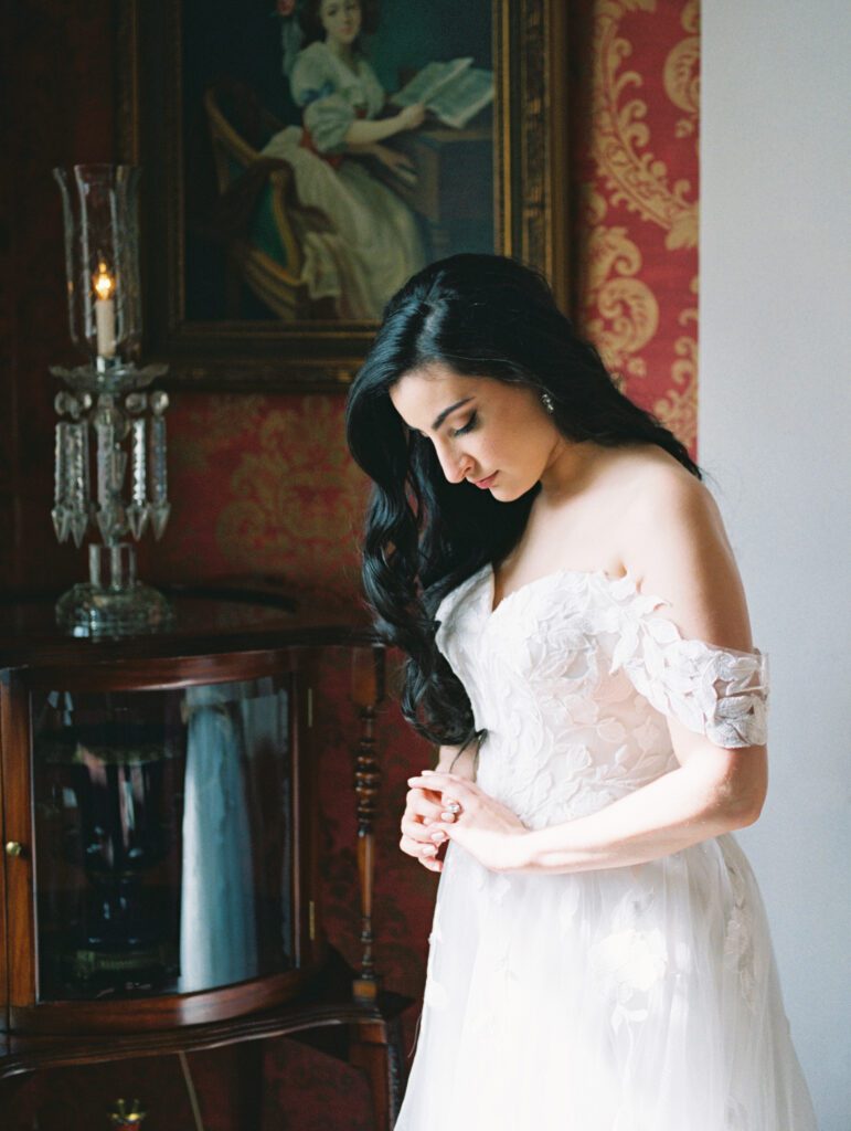 A bride pauses to admire her ring while she waits for weather to pass before her ceremony at a historical venue full of antiques