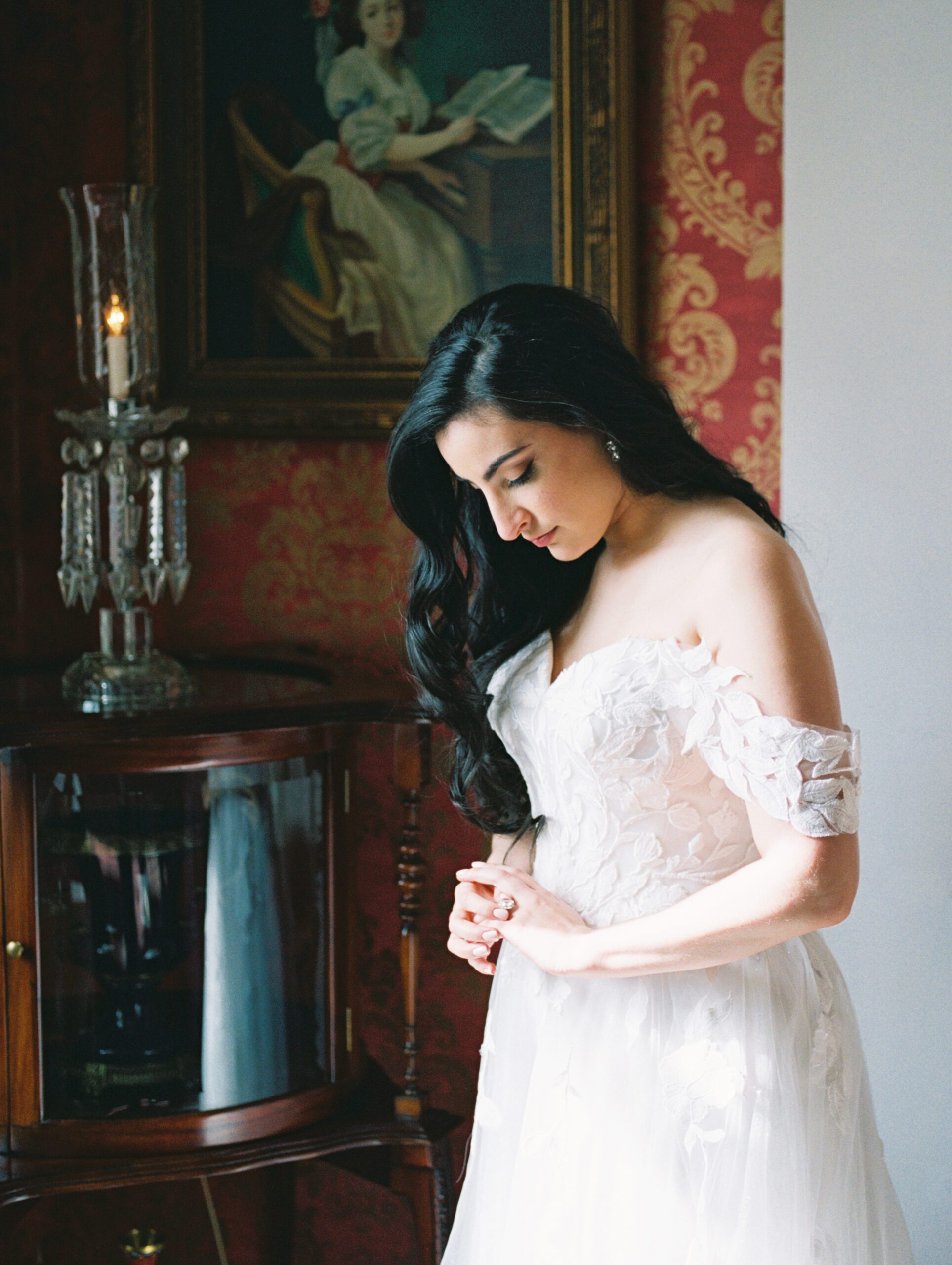 A bride pauses to admire her ring while she waits for weather to pass before her ceremony at a historical venue full of antiques